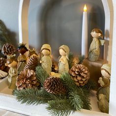 a mantle with pine cones, candles and figurines sitting on top of it