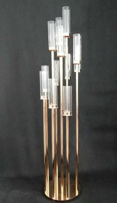 a tall metal and glass candle holder with six candles in the center on a black background