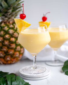 two glasses filled with pineapple drink and topped with cherries