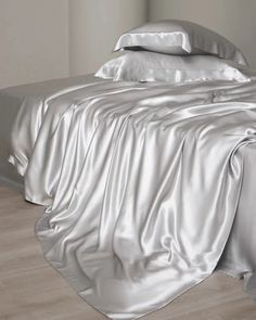 an unmade bed with silver sheets and pillows