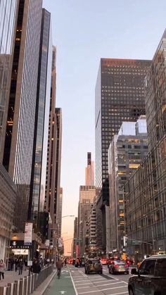 a city street filled with lots of tall buildings next to traffic and people walking on the sidewalk