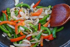 stir fry vegetables being cooked in a wok with a wooden spoon on the side