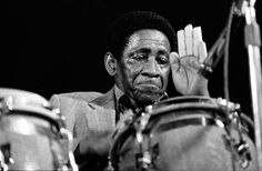 a black and white photo of a man holding his hands up to his face while playing the drums