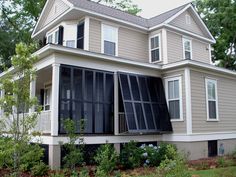 a large house with many windows and shutters on the front porch, next to some trees