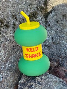 a green cup sitting on top of a rock next to a yellow straw in it