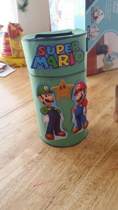 a cup with mario and luigi on it sitting on top of a wooden table next to a cardboard box