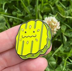 a hand holding a yellow pin with an image of a jellyfish on it