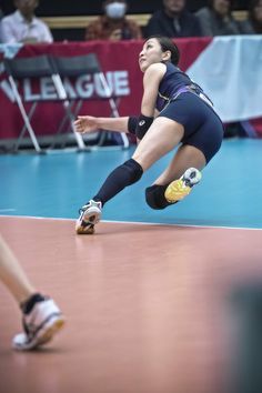 a female volleyball player dives for the ball during a match in front of an audience