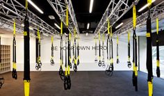 an empty gym room with yellow and black ropes hanging from the ceiling, in front of a white wall