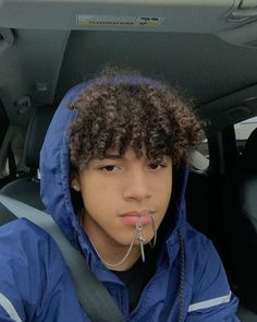 a young man with curly hair wearing a blue jacket in the back seat of a car