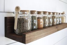 there are many jars with spices on the shelf next to each other and one is holding a wooden spoon