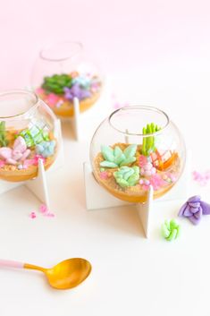 two fish bowls filled with plants and rocks on top of a white table next to a spoon