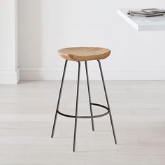 a wooden stool sitting on top of a hard wood floor next to a white wall