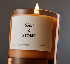 a candle with salt and stone written on the front is lit up against a gray background