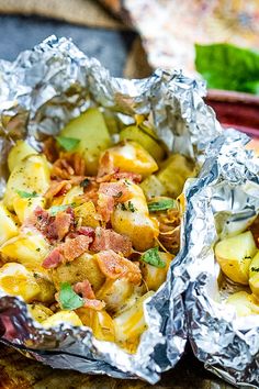 two foil packets filled with potatoes and bacon on top of a wooden table next to a plate