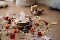 an arrangement of flowers and candles on the floor in front of a clock with petals scattered all over it