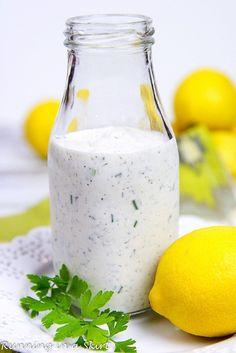 a glass bottle filled with white sauce next to lemons and parsley on a doily