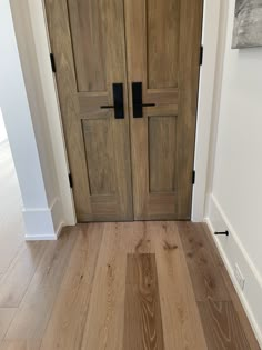 a wooden door with two black handles in a white walled entryway to a home