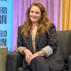 a woman sitting on top of a couch in front of a blue and purple curtain