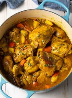 a pot filled with chicken and vegetables on top of a white wooden table next to a blue spoon