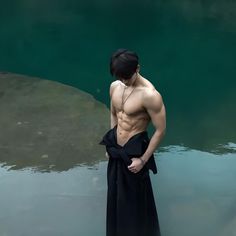 a shirtless man standing in the water with his hands on his hips and looking down