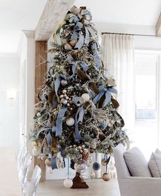 a decorated christmas tree in the middle of a living room with blue ribbon on it