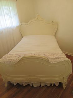 a white bed sitting on top of a hard wood floor next to a window with sheer curtains