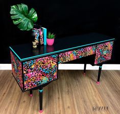 a black desk with colorful leopard print on it and two plants sitting on top of it