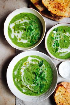 three bowls filled with green soup on top of a white plate next to some bread