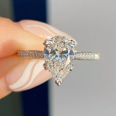 a close up of a person's hand holding a ring with a pear shaped diamond