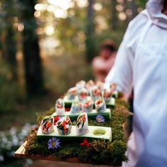 there are many sushi rolls on the tray in the forest with moss and flowers