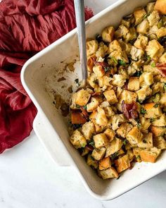 a white bowl filled with stuffing next to a red napkin and spoon on top of a table