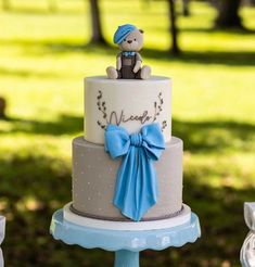 a blue and white wedding cake with a teddy bear on top is sitting on a stand