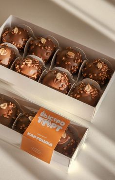 a box of chocolate truffles with nuts on top sitting on a white table