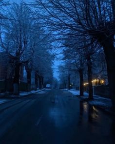 an empty street at night with snow on the ground and trees in the foreground