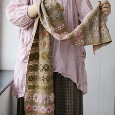 a woman wearing a pink shirt and holding a scarf over her shoulder with both hands