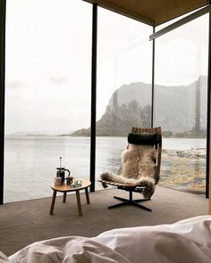 a bedroom with a chair and table in front of a window looking out onto the water