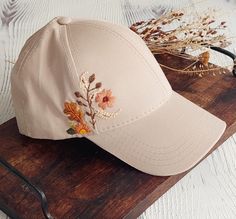 a baseball cap with embroidered flowers on it sitting on top of a wooden cutting board