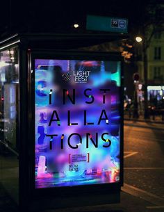 a bus stop sign on the side of a city street at night with lights in the background