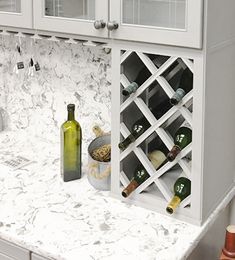 a kitchen with marble counter tops and white cupboards filled with wine bottles on it