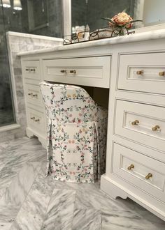 a chair sitting in the corner of a bathroom under a vanity with flowers on it