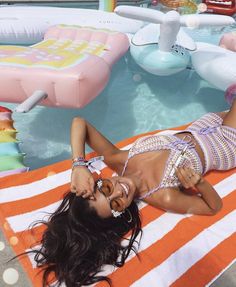 a woman laying on top of an orange and white towel next to a swimming pool