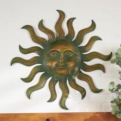 a metal sun face mounted to the side of a white wall next to a potted plant