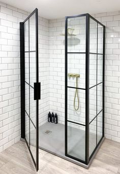 a bathroom with a glass shower stall and white brick walls, along with wooden flooring