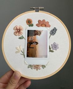 a hand holding up a white embroidery hoop with flowers on it and a photo in the center