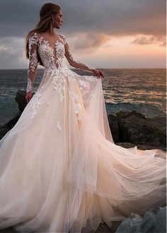 a woman in a wedding dress standing on the rocks by the ocean with her back to the camera