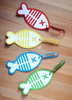 three fish shaped paper clips sitting on top of a wooden table next to each other