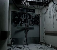 an abandoned room with graffiti on the walls and floor, including wires hanging from the ceiling