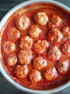 meatballs covered in marinara sauce in a white bowl on a wooden table top