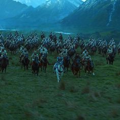 a large group of people on horses in the grass with mountains in the back ground